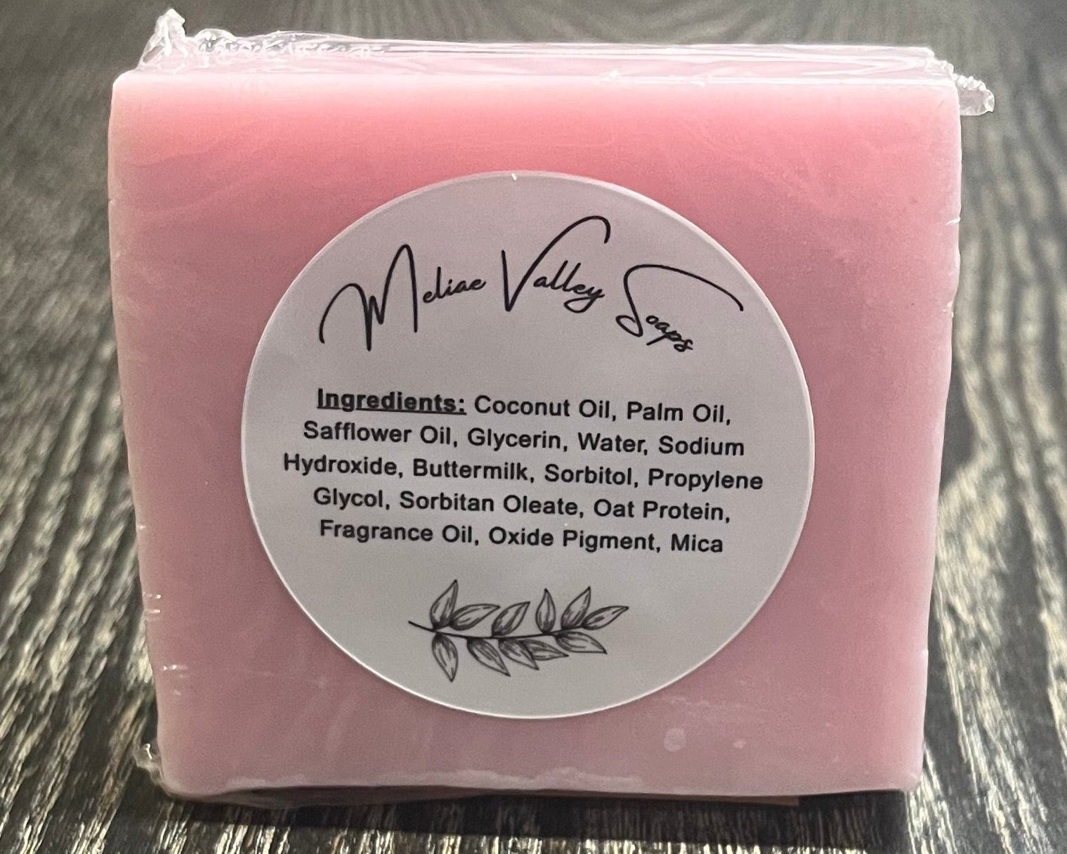Pink soap bar with a label on a wooden surface.