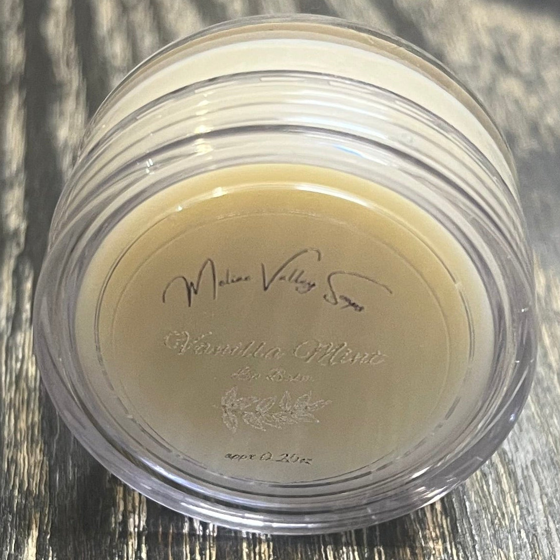 A lip pot filled with lip balm. The lip pot is positioned on its side with its label facing the camera. 