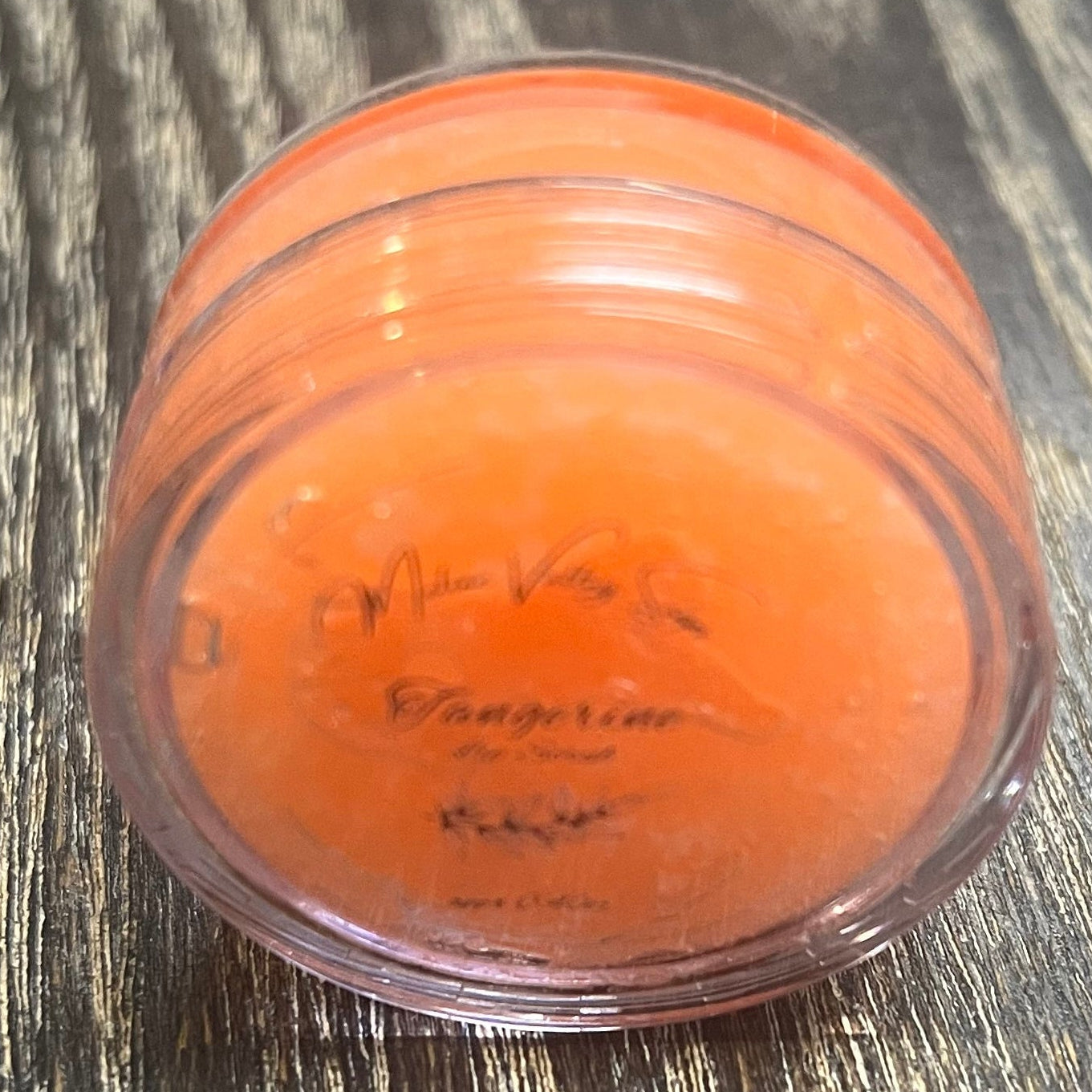 A lip pot filled with sugar dyed orange. The lip pot is positioned on its side with its label facing the camera. 