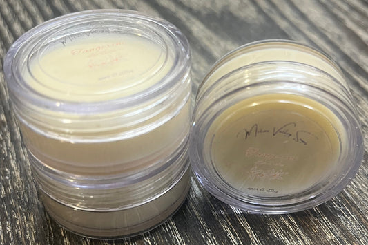 Three lip pots filled with lip balm. On the left-hand side, two of the lip pots are stacked. On the right-hand side, the third lip pot is positioned on its side with its label facing the camera. 