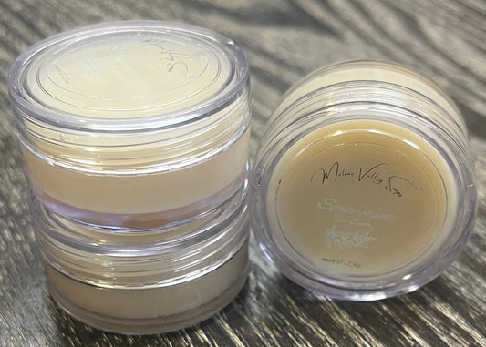 Three lip pots filled with lip balm. On the left-hand side, two of the lip pots are stacked. On the right-hand side, the third lip pot is positioned on its side with its label facing the camera. 