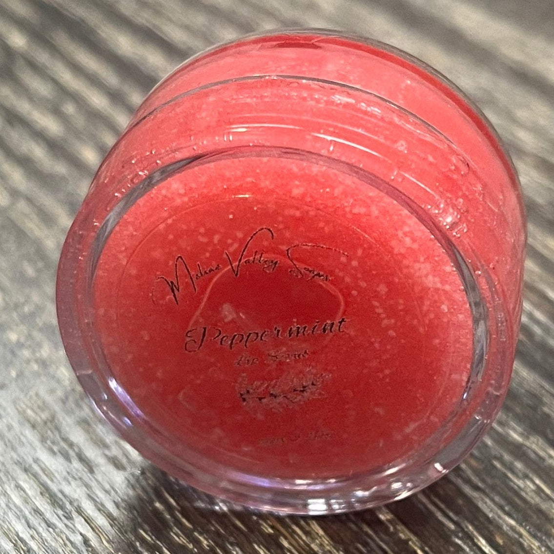 A lip pot filled with sugar dyed red. The lip pot is positioned on its side with its label facing the camera. 
