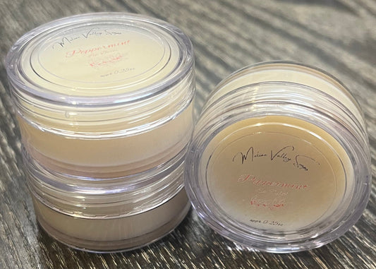 Three lip pots filled with lip balm. On the left-hand side, two of the lip pots are stacked. On the right-hand side, the third lip pot is positioned on its side with its label facing the camera. 