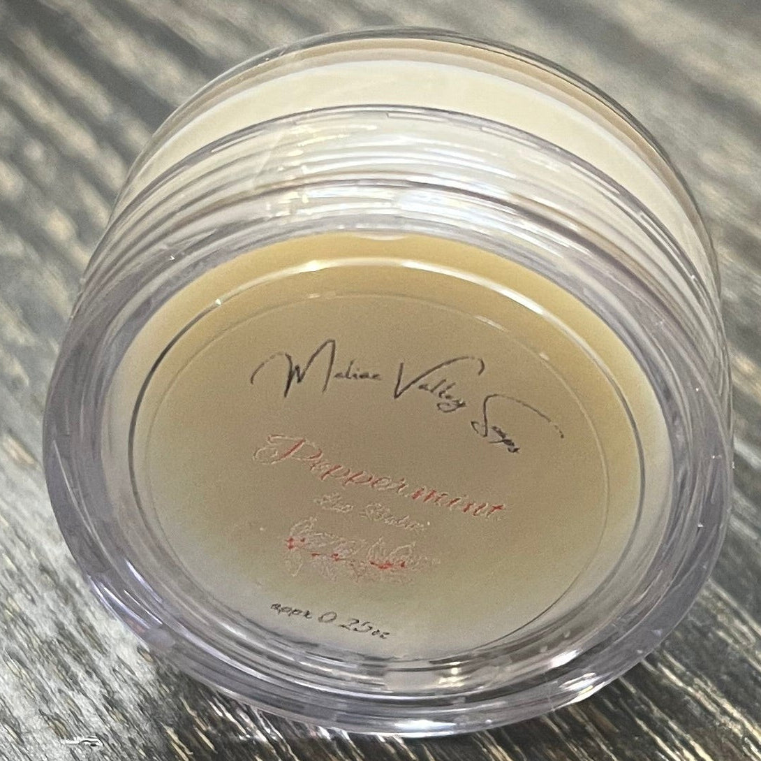 A lip pot filled with lip balm. The lip pot is positioned on its side with its label facing the camera. 