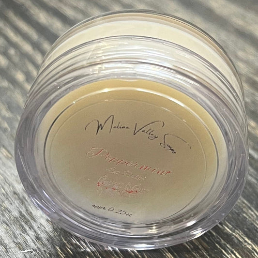 A lip pot filled with lip balm. The lip pot is positioned on its side with its label facing the camera. 