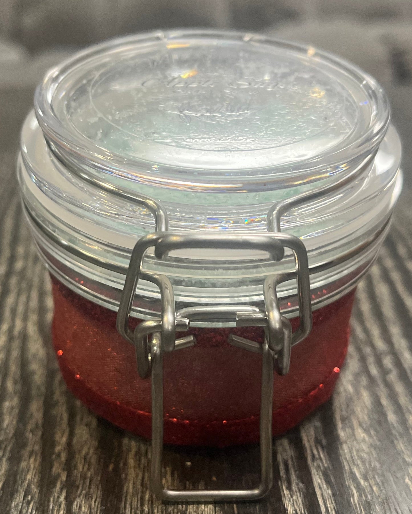 Clear round jar with a sticker on top. You see the side of the jar, which is covered in a sparkly red ribbon. 