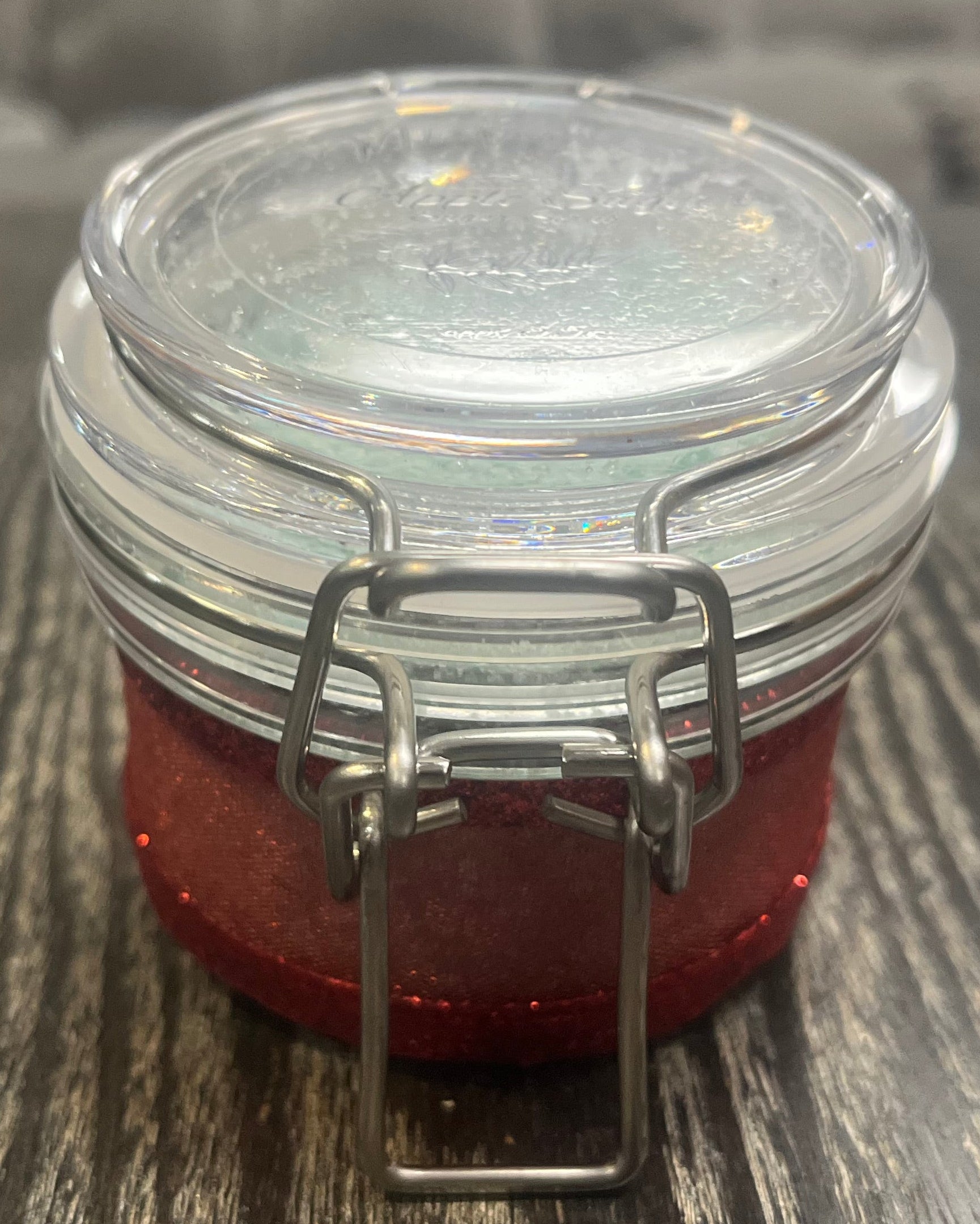Clear round jar with a sticker on top. You see the side of the jar, which is covered in a sparkly red ribbon. 