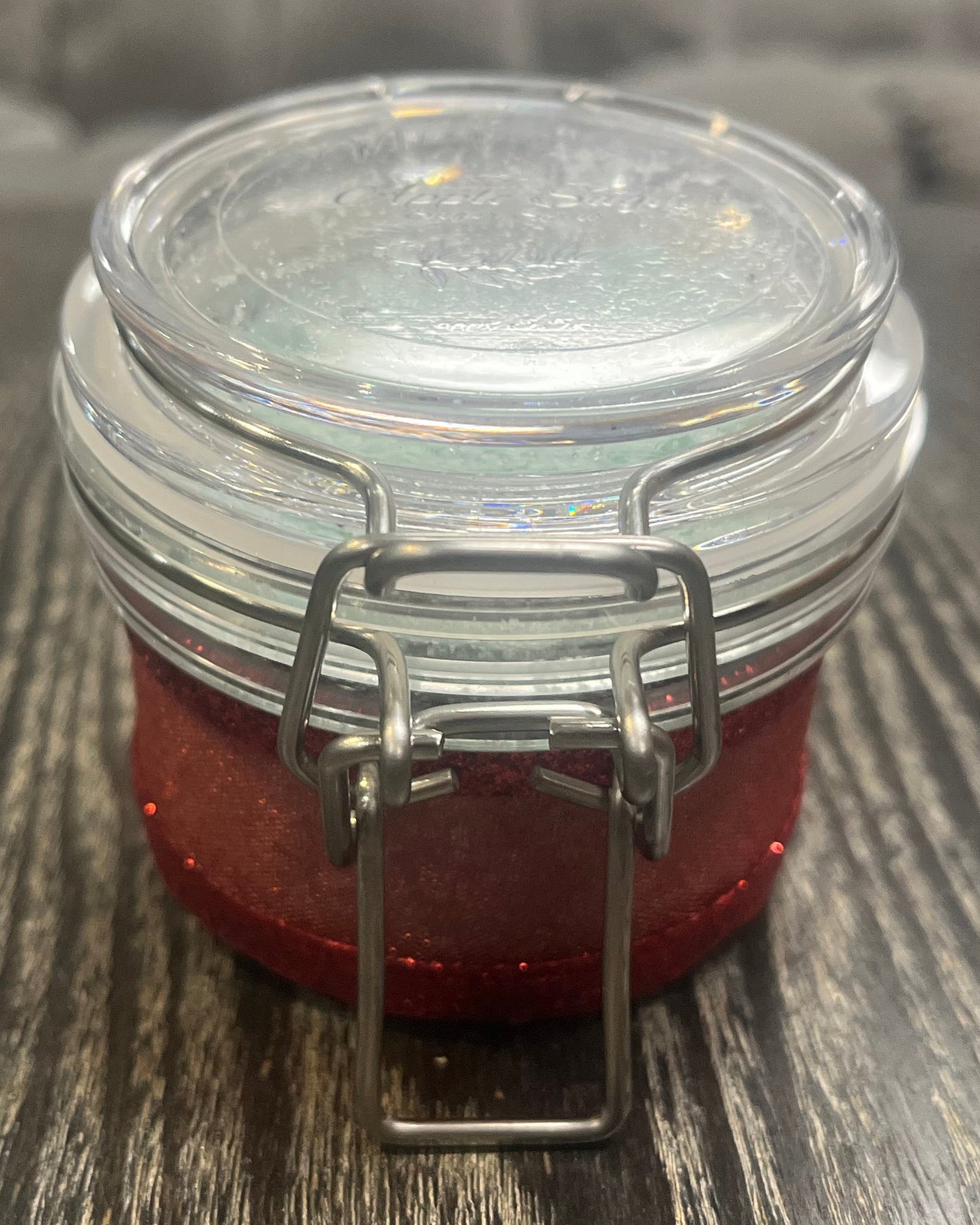 Clear round jar with a sticker on top. You see the side of the jar, which is covered in a sparkly red ribbon. 