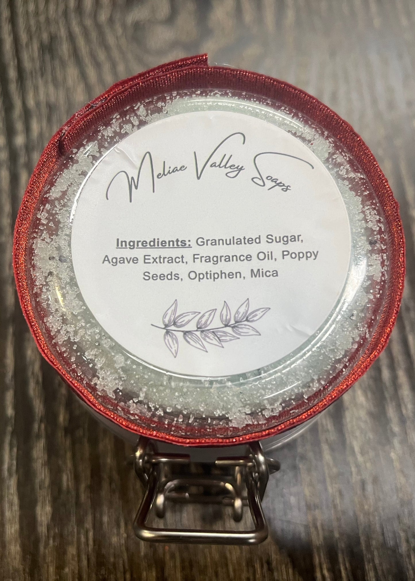 The bottom of a jar with a red ribbon around it. The bottom of the jar has a white sticker with the ingredients on it. 