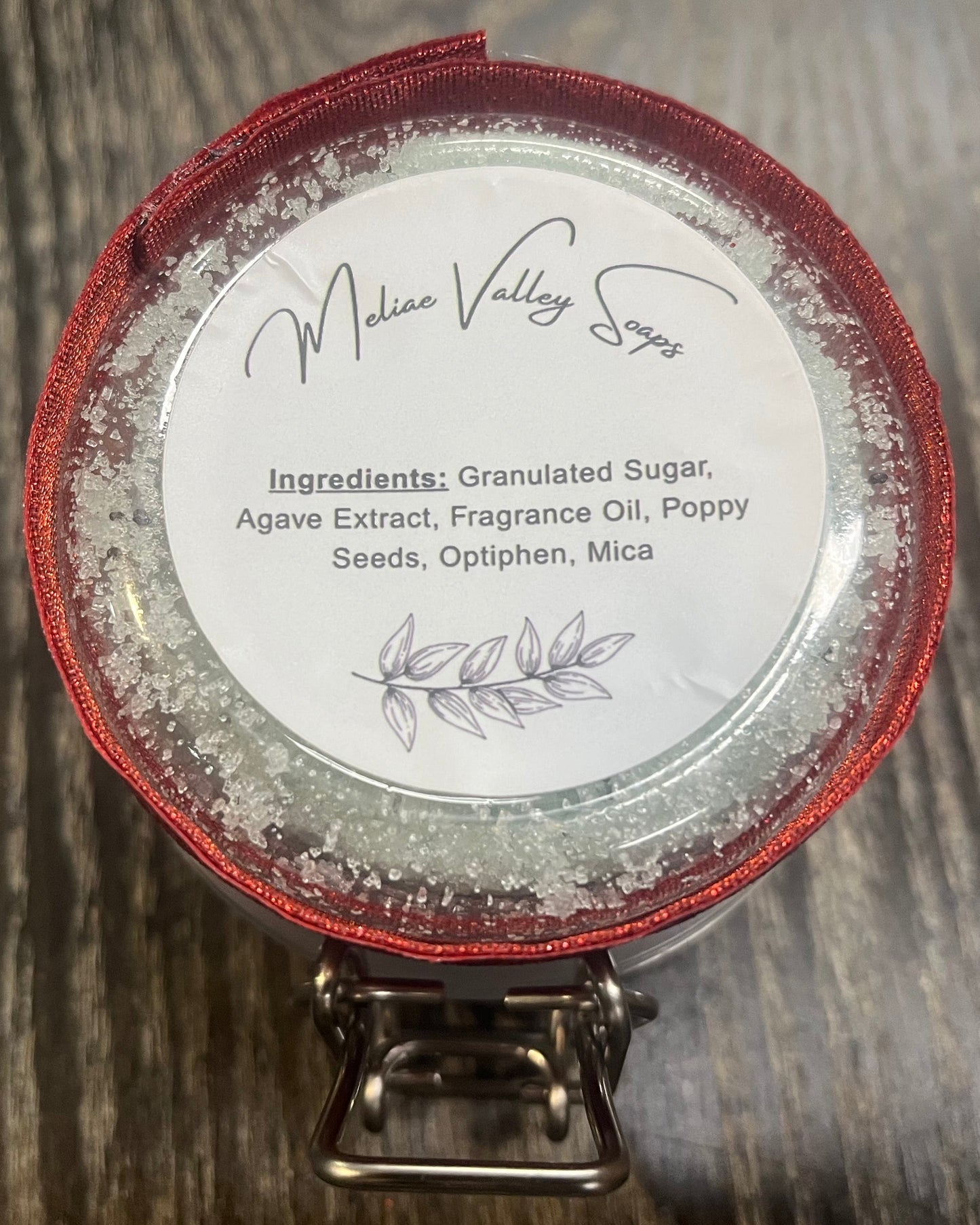 The bottom of a jar with a red ribbon around it. The bottom of the jar has a white sticker with the ingredients on it. 