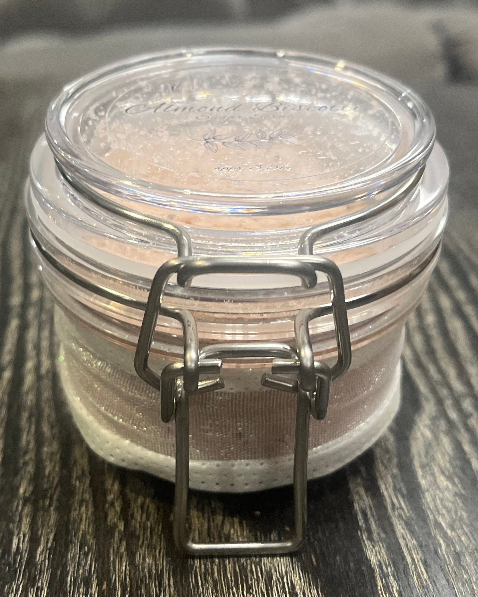 Clear round jar with a sticker on top. You see the side of the jar, which is covered in a sparkly white ribbon. 