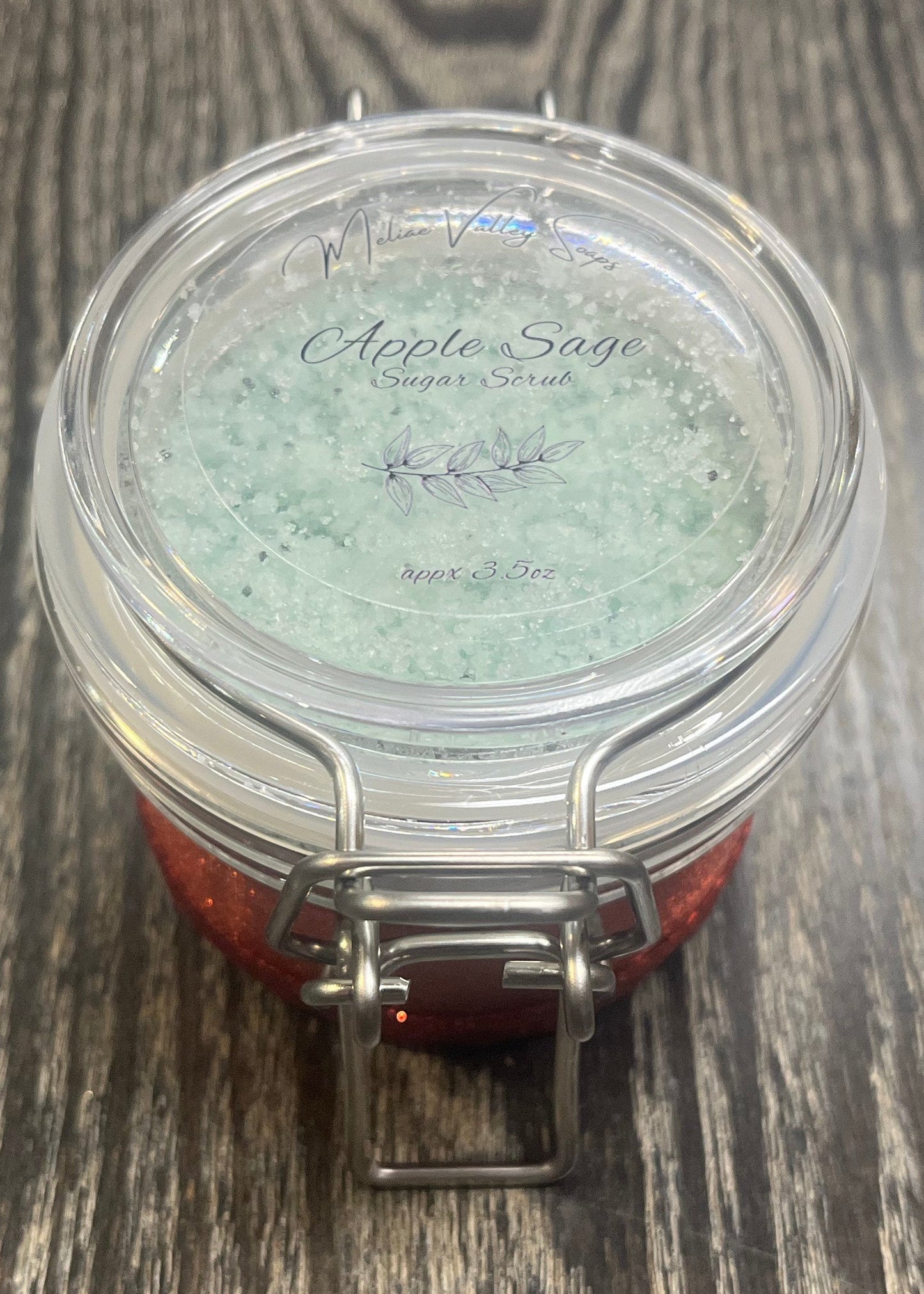 Clear round jar with a sticker on top. You see through the jar to green sugar. 