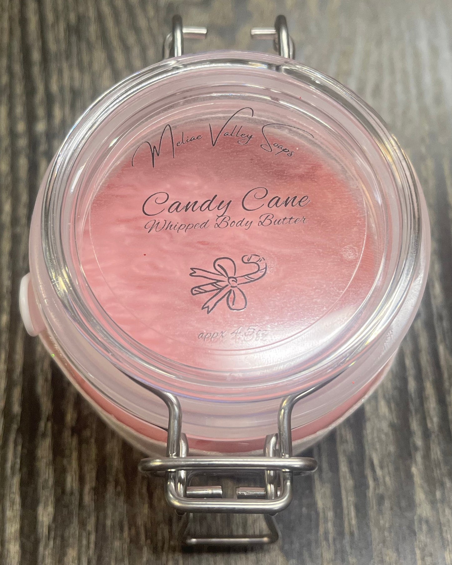 Clear round jar with a sticker on top. You see through to the jar of pink body butter. 