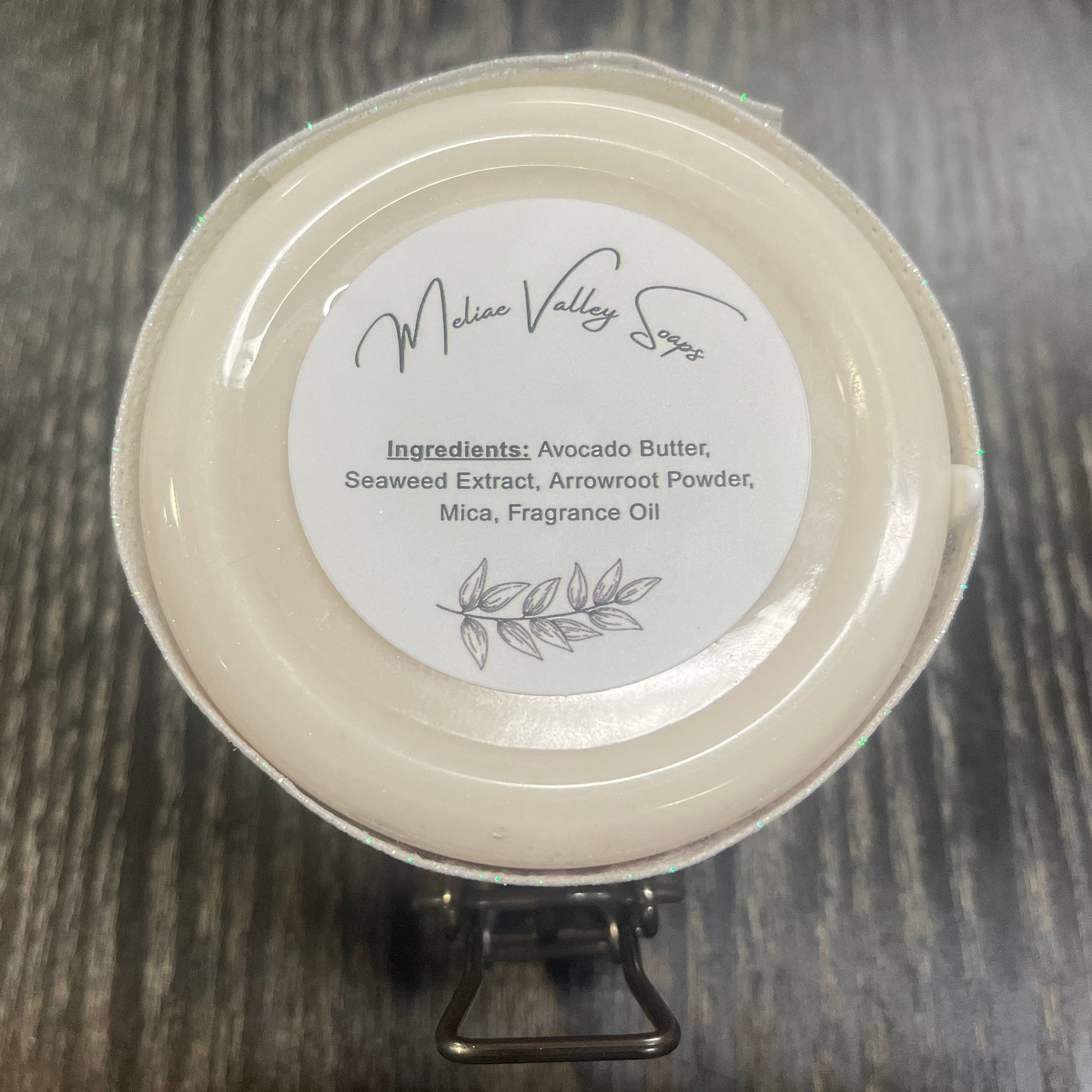 The bottom of a jar with a white ribbon around it. The bottom of the jar has a white sticker with the ingredients on it. 