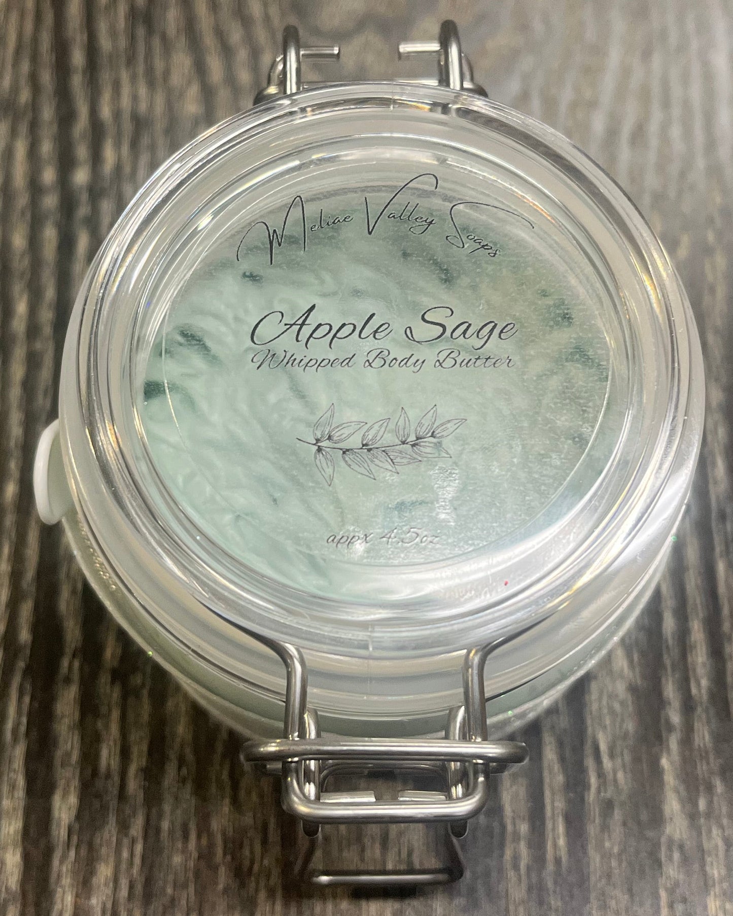 Clear round jar with a sticker on top. You see through to the jar to green body butter. 