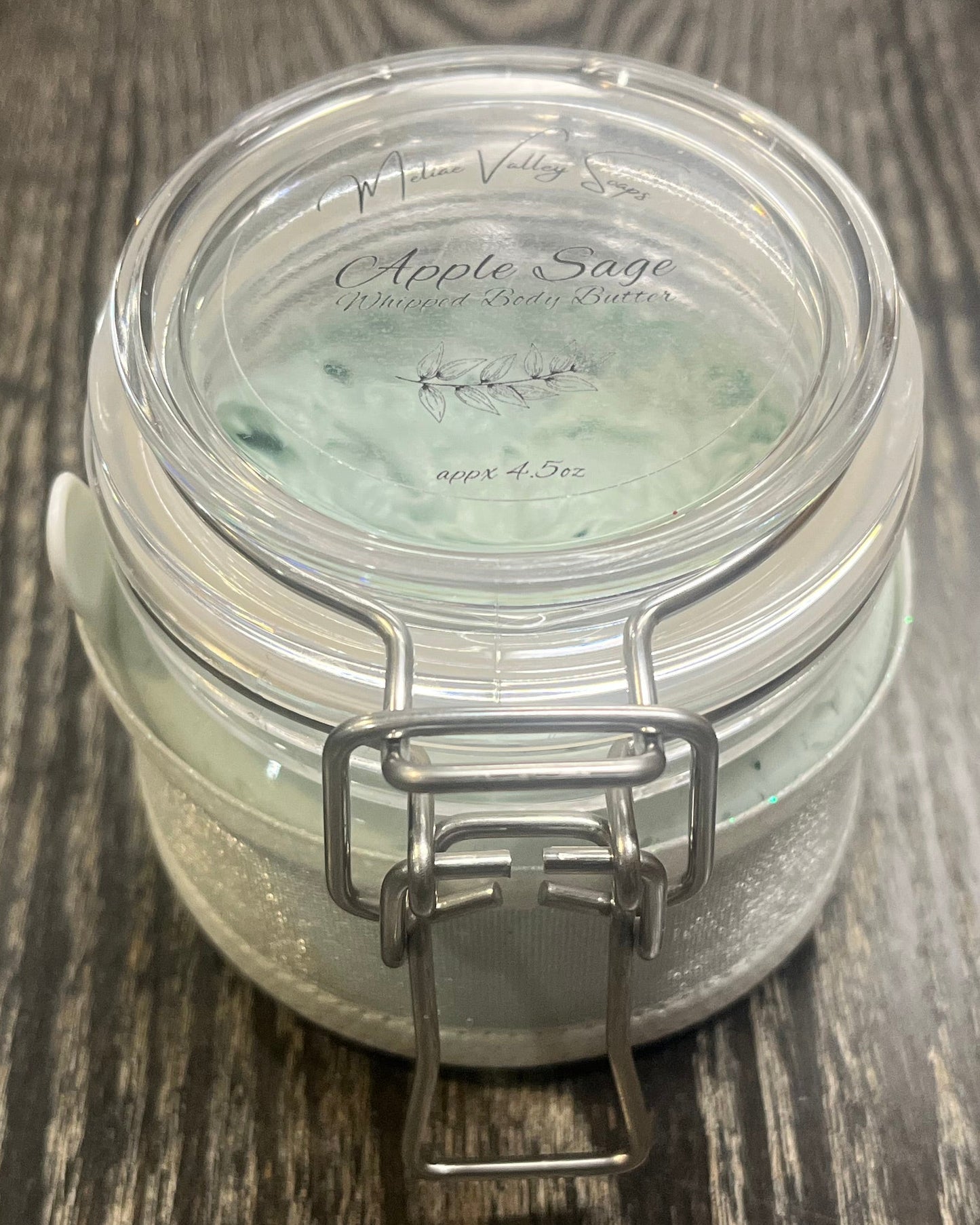 Clear round jar with a sticker on top. You see through to the jar to green body butter. 