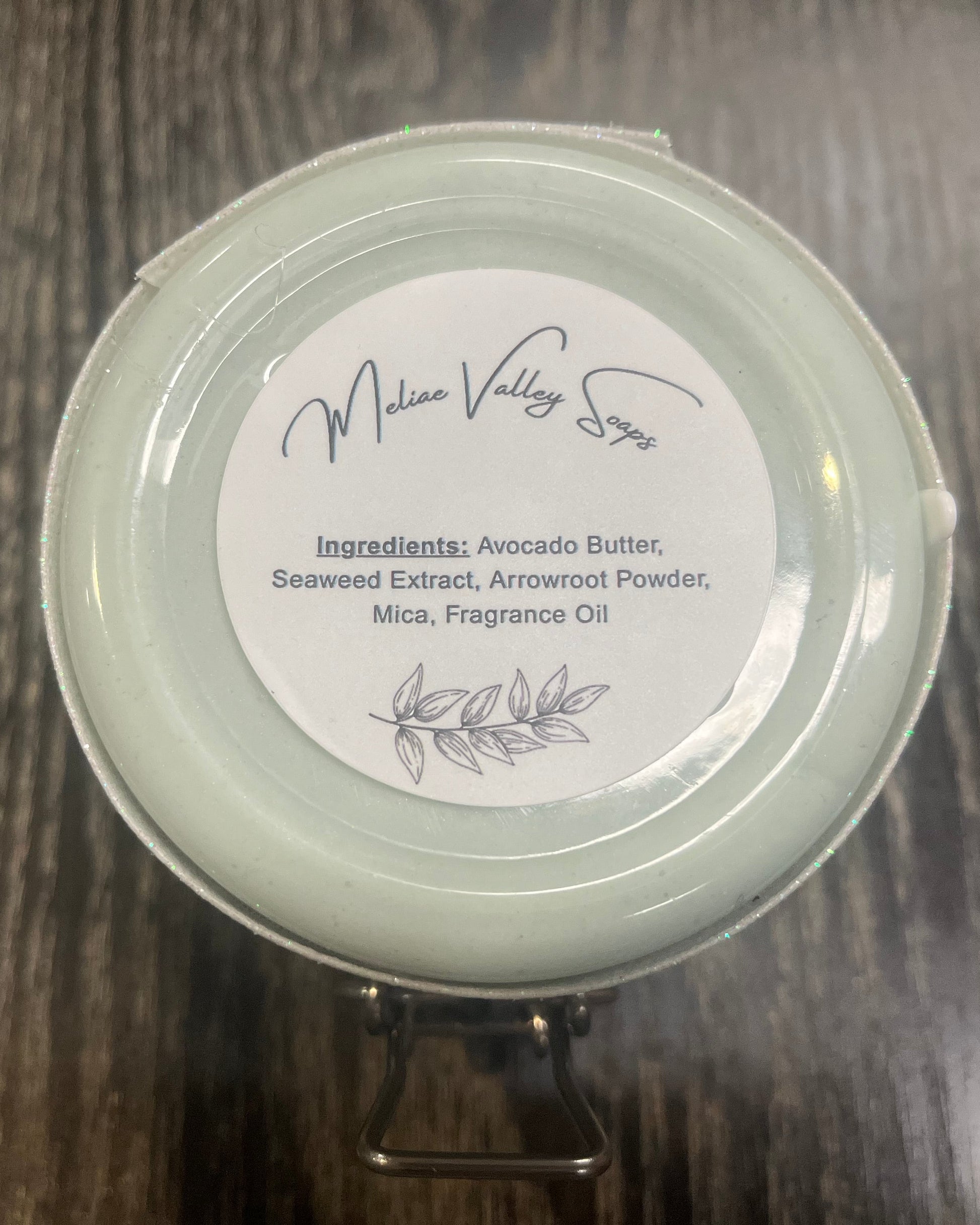 The bottom of a jar with a white ribbon around it. The bottom of the jar has a white sticker with the ingredients on it. 