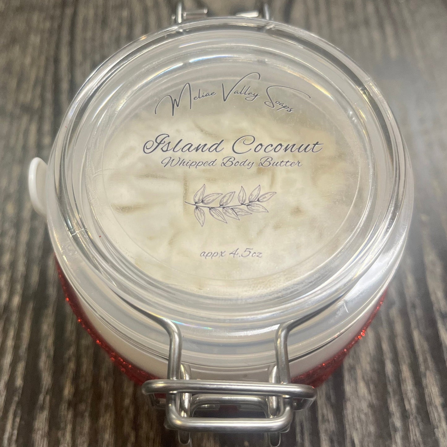 Clear round jar with a sticker on top. You see through to the jar to white body butter. 