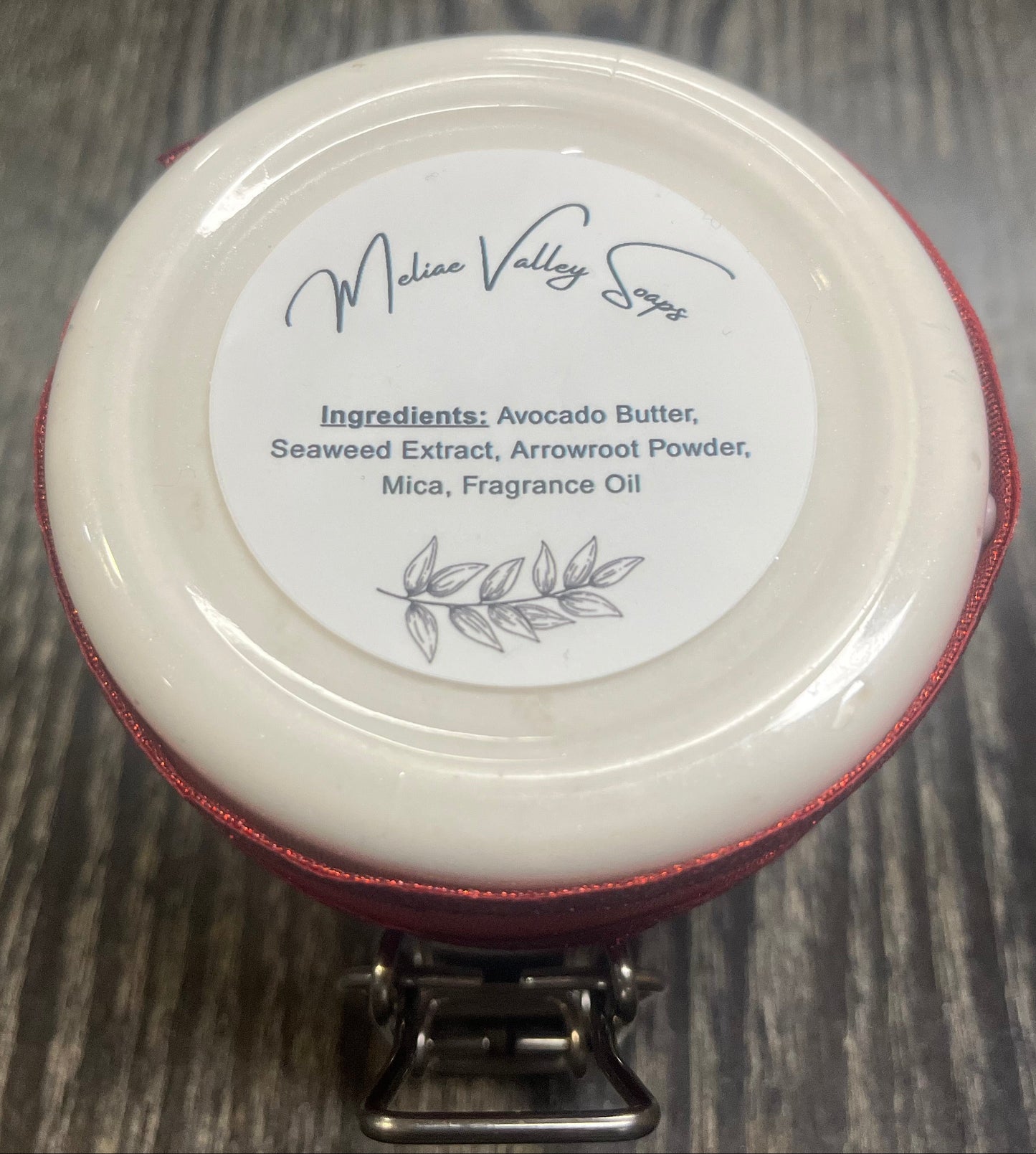The bottom of a jar with a red ribbon around it. The bottom of the jar has a white sticker with the ingredients on it. 