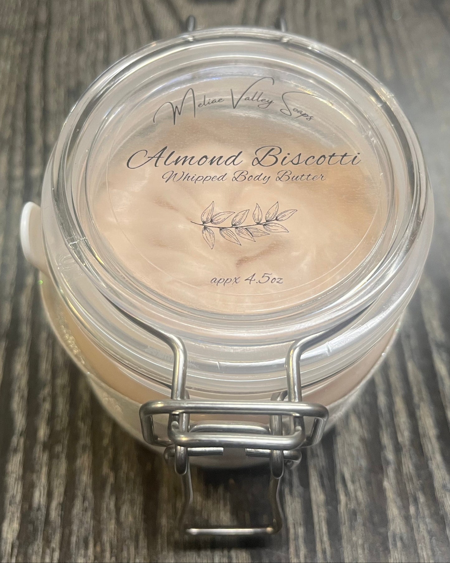 Clear round jar with a sticker on top. You see through to the jar of bronze body butter. 