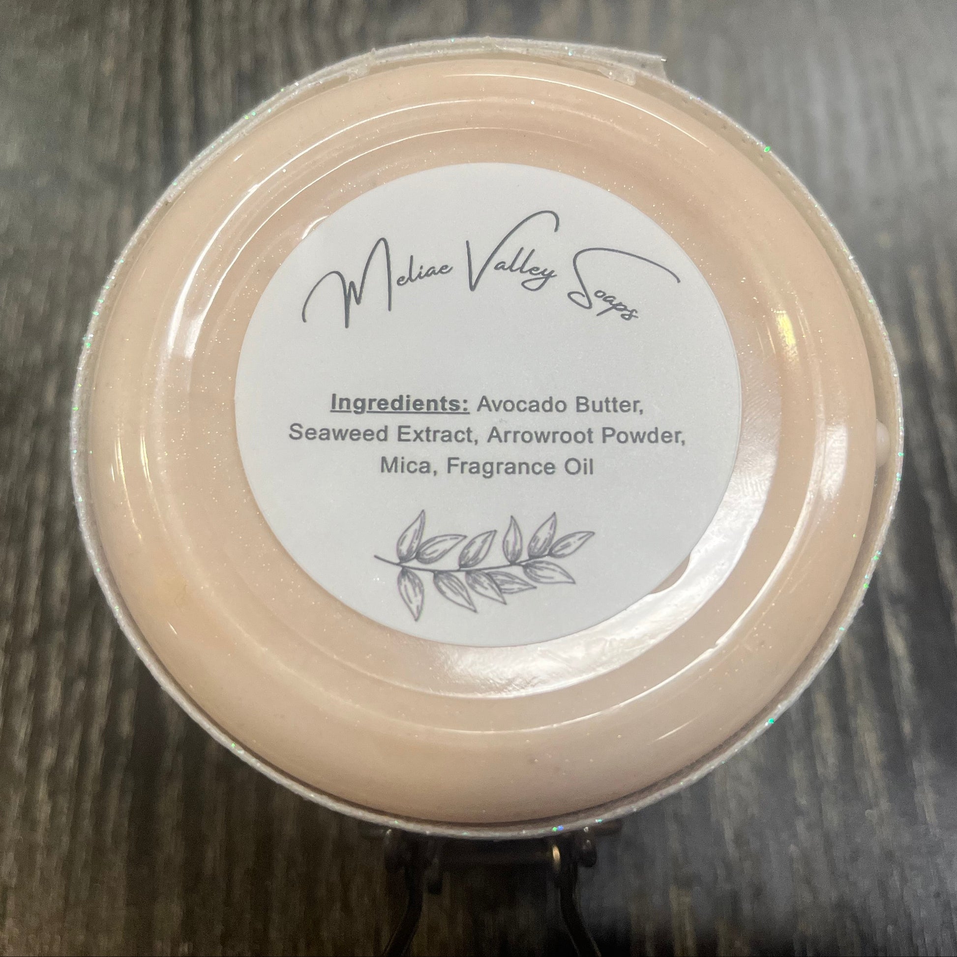 The bottom of a jar with a white ribbon around it. The bottom of the jar has a white sticker with the ingredients on it. 