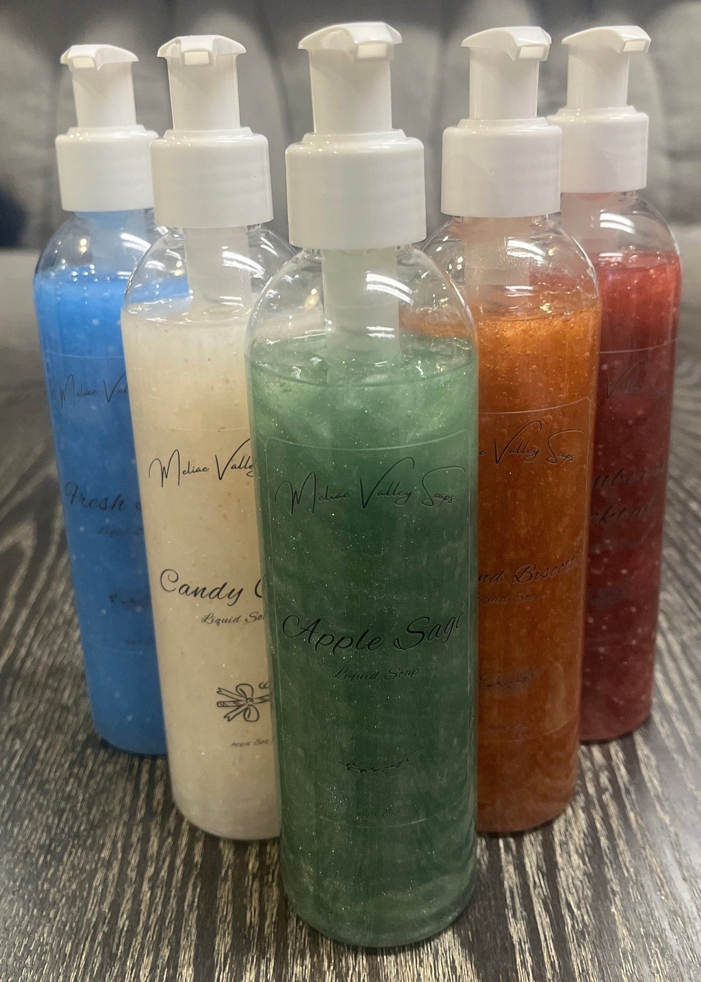 A set of pump bottles with different colored liquids, bronze, white, blue, red, and green, in a 'V' shape on a wooden surface. 