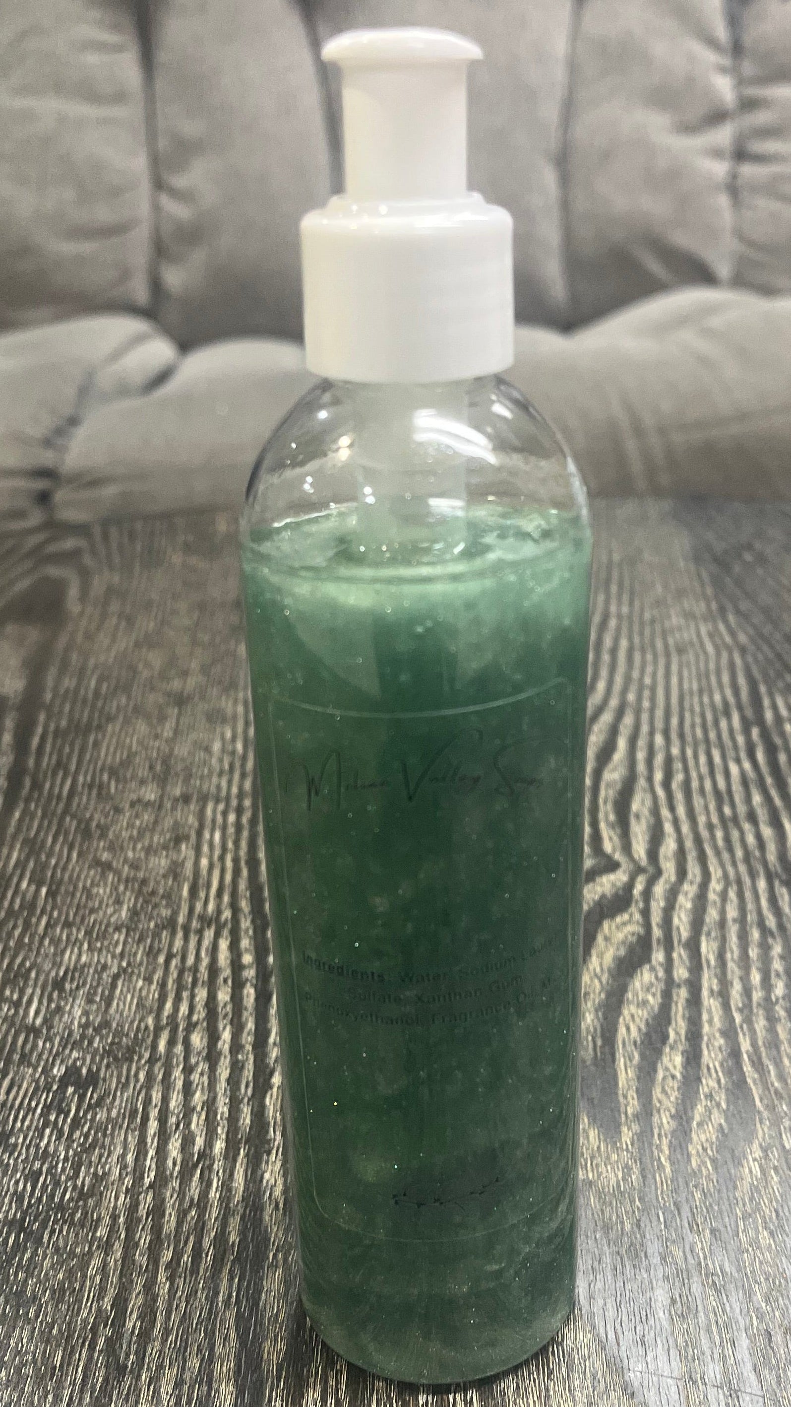 A clear pump bottle with a white nozzle full of green liquid on a textured surface. 