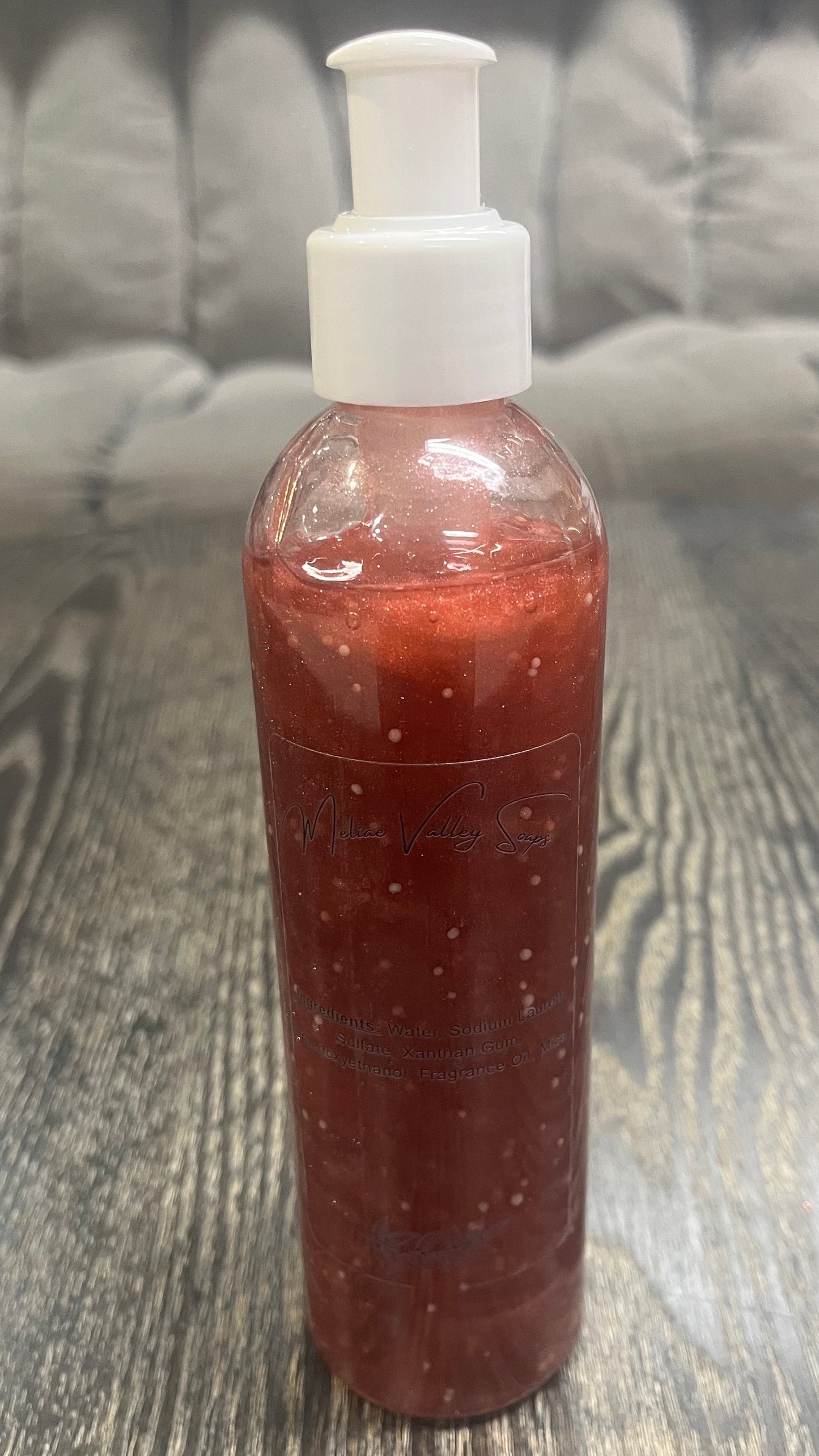 A clear pump bottle with a white nozzle full of red liquid with white beads on a textured surface. 