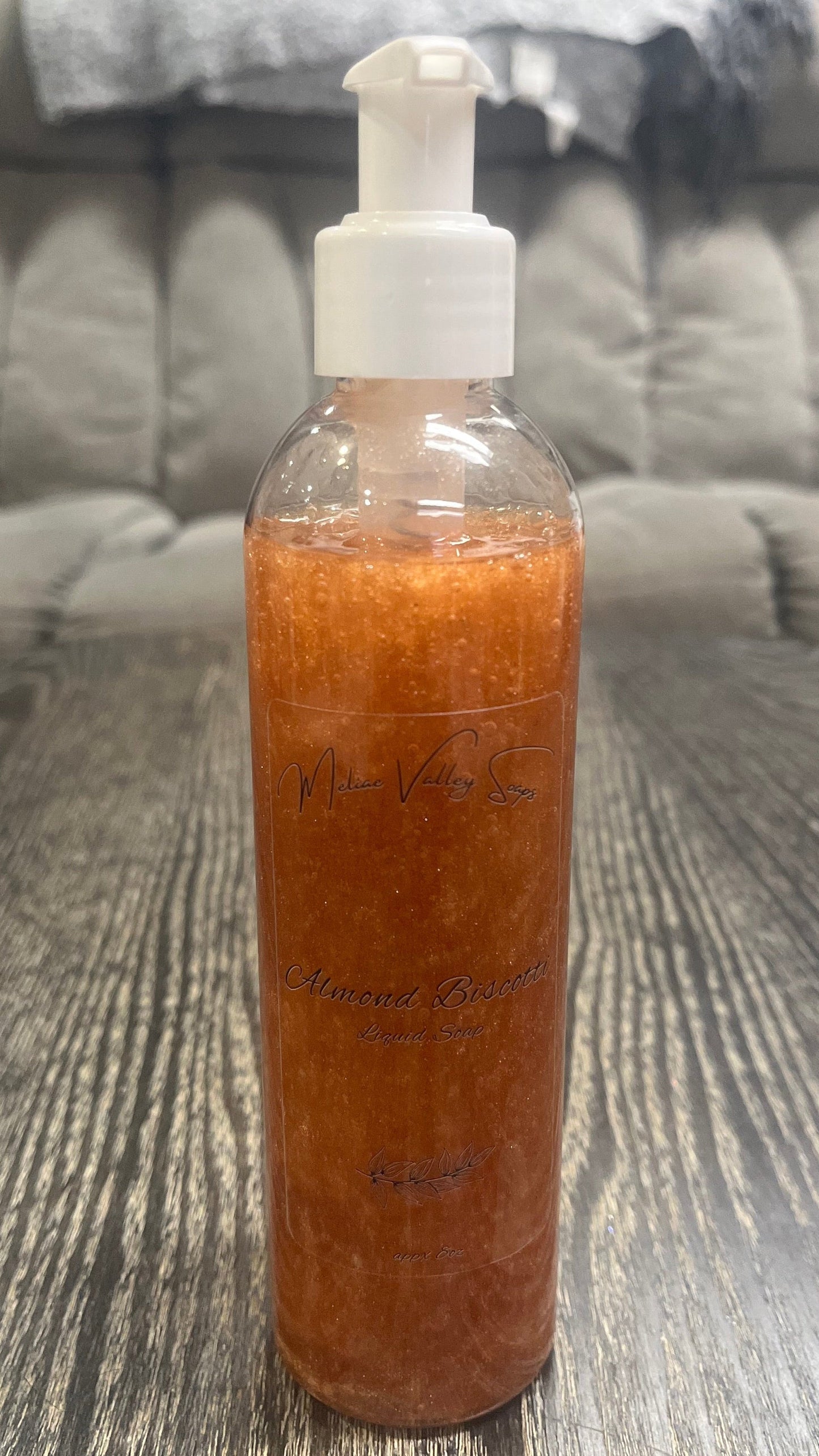 A clear pump bottle with a white nozzle full of bronze liquid on a textured surface. 