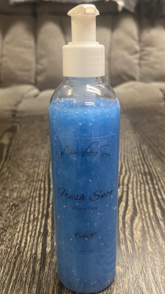 A clear pump bottle with a white nozzle full of blue liquid with white beads on a textured surface. 