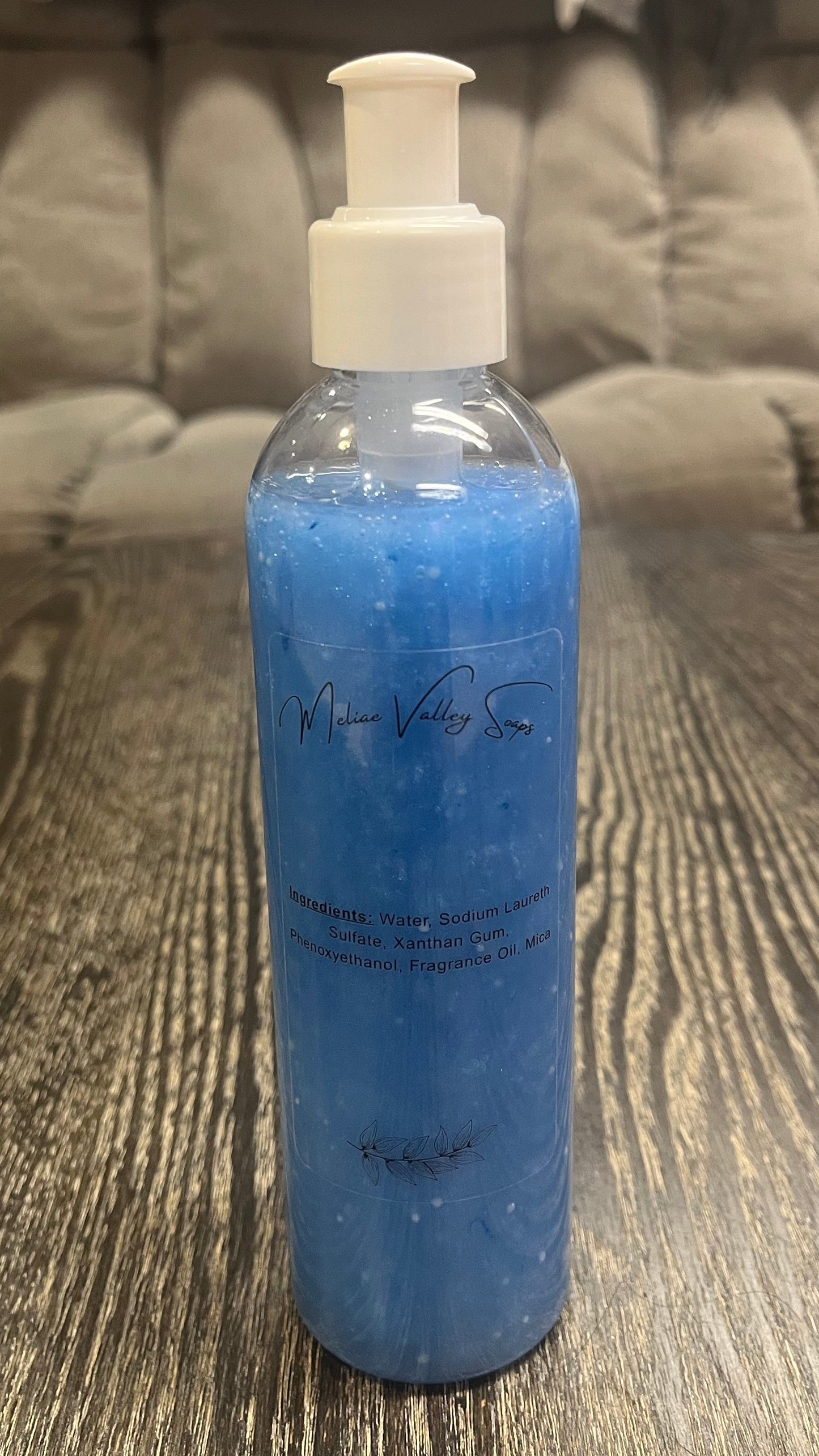 A clear pump bottle with a white nozzle full of blue liquid with white beads on a textured surface. 