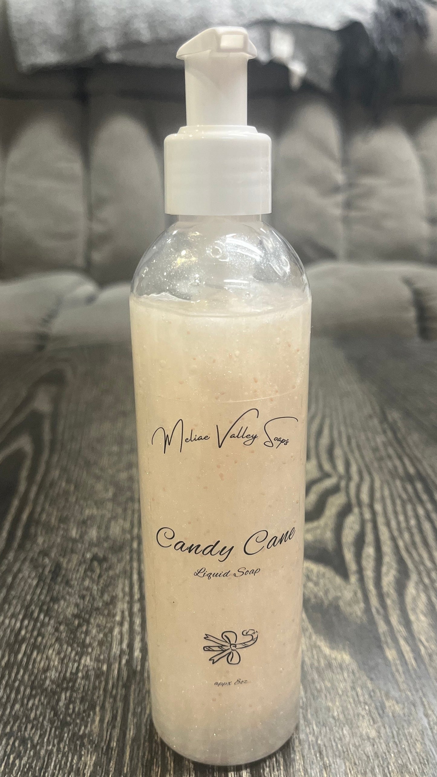 A clear pump bottle with a white nozzle full of white liquid with pink beads on a textured surface. 