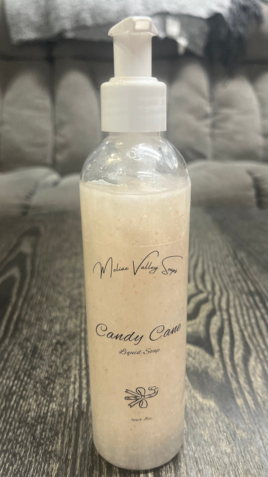 A clear pump bottle with a white nozzle full of white liquid with pink beads on a textured surface. 