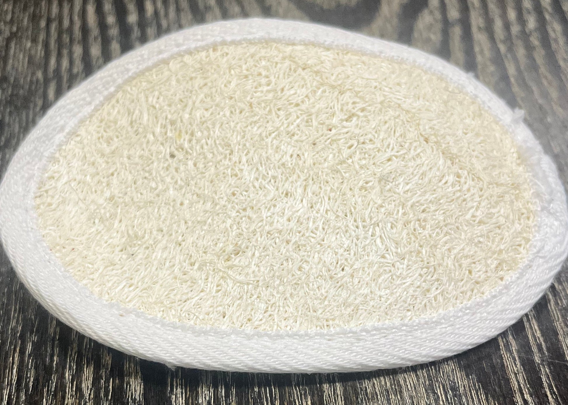 Round, white, textured loofah pad on a dark wooden surface. 