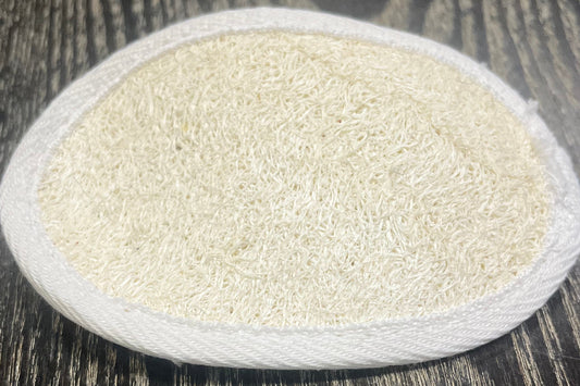 Round, white, textured loofah pad on a dark wooden surface. 