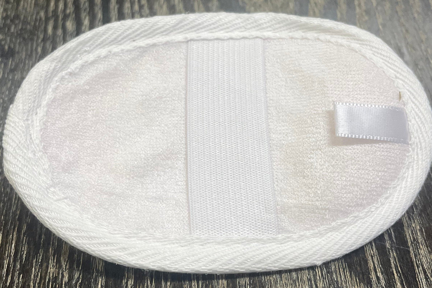 Round, white, loofah pad with an elastic band on a dark wooden surface.