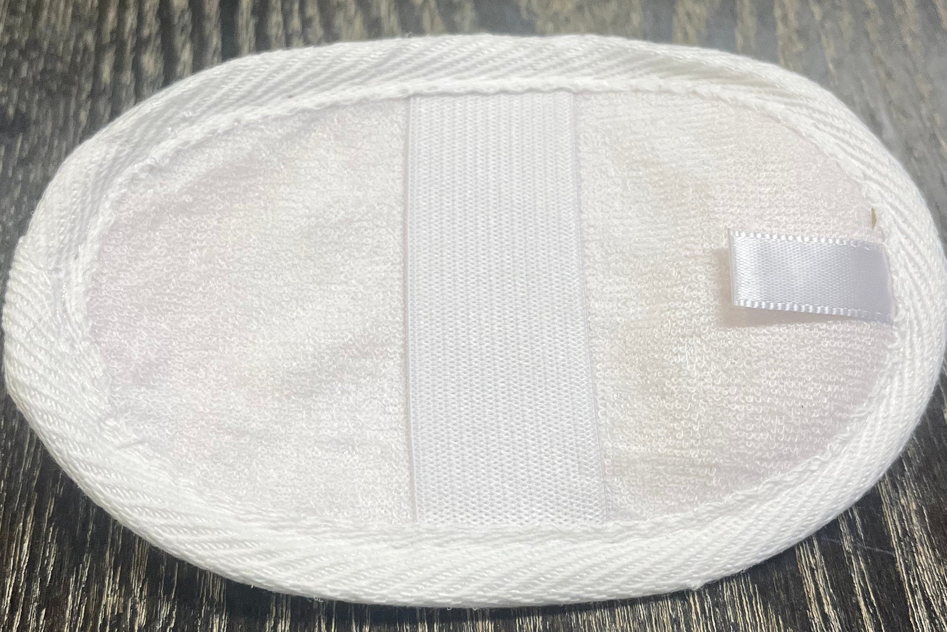 Round, white, loofah pad with an elastic band on a dark wooden surface.