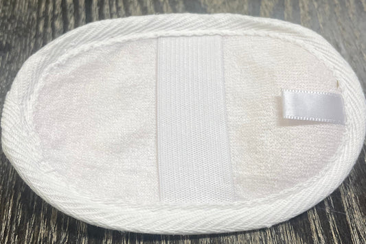 Round, white, loofah pad with an elastic band on a dark wooden surface.
