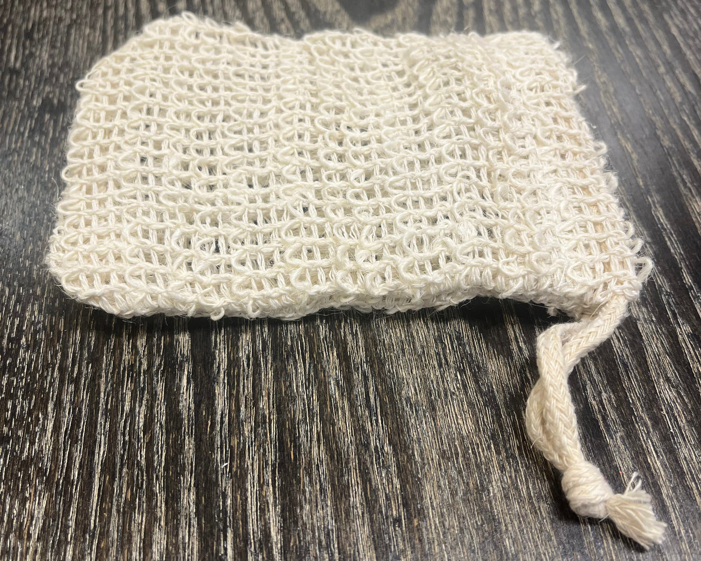 Beige woven exfoliating soap bag on a dark wooden surface. 