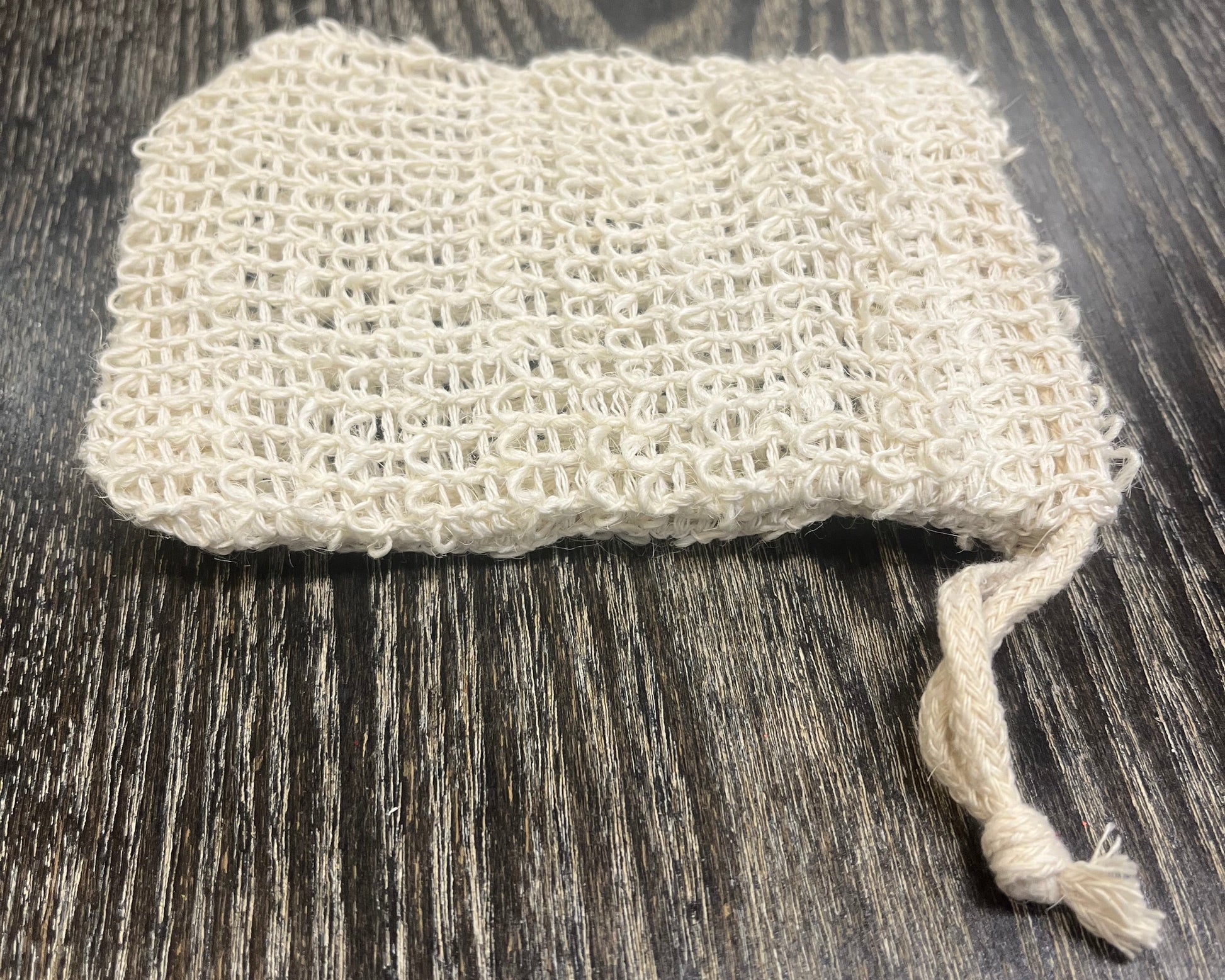 Beige woven exfoliating soap bag on a dark wooden surface. 