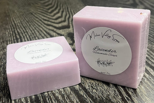 Two bars of purple soap with white labels on a textured surface. One is lying down, and the other is upright on its side. 