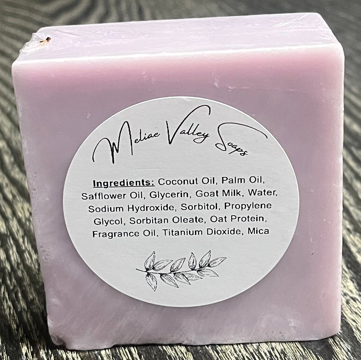 A purple bar of soap with a white ingredients label on a wooden surface. 