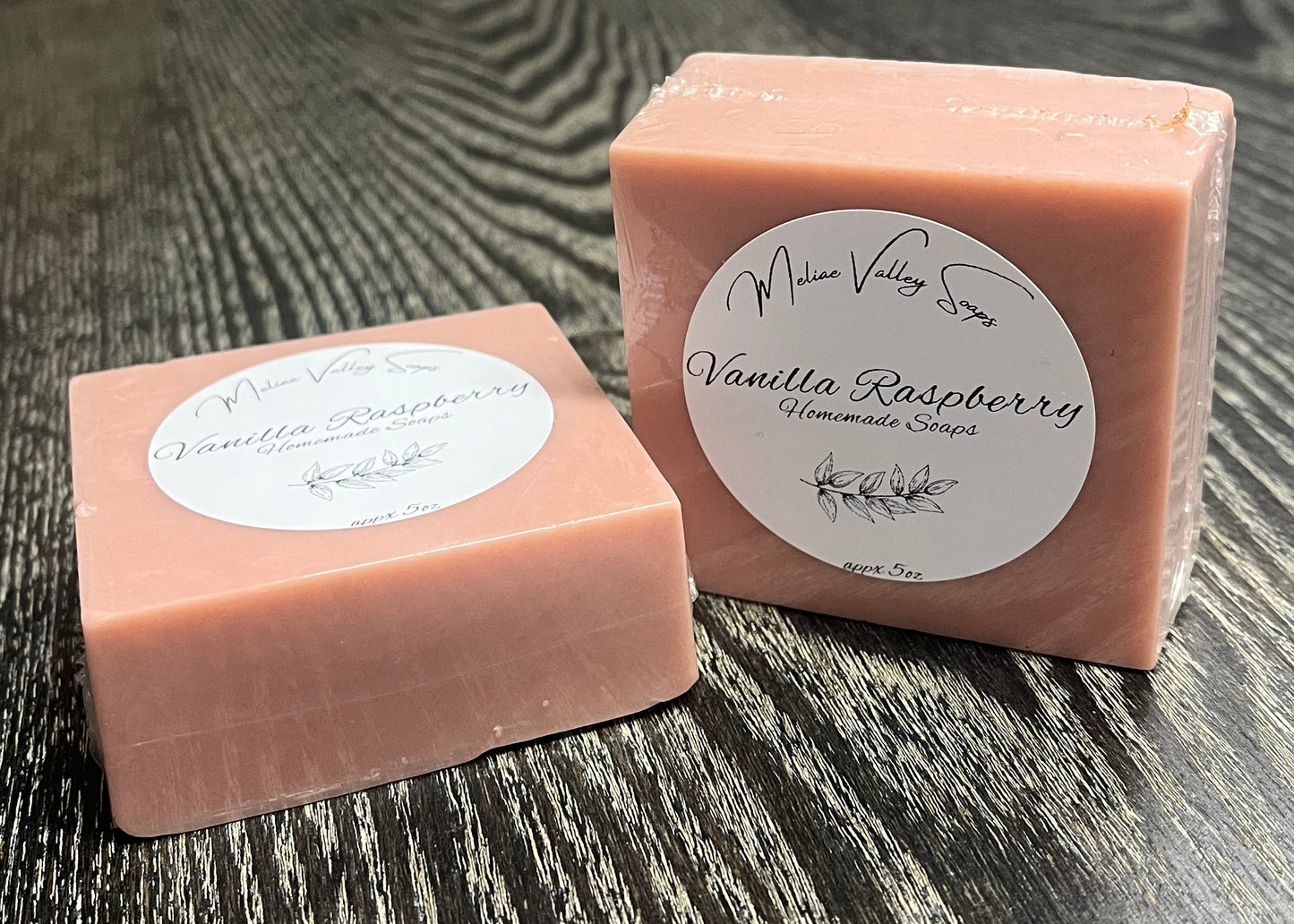 Two pink bars of soap with labels on a wooden surface. One is lying down, and the other is upright. 