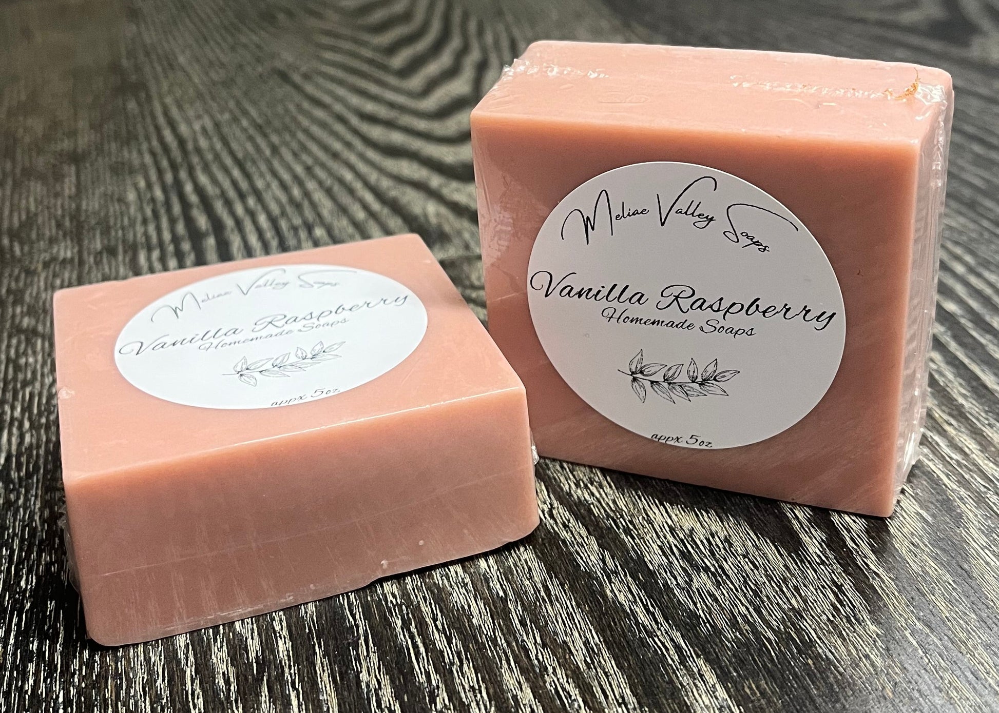 Two pink bars of soap with labels on a wooden surface. One is lying down, and the other is upright. 