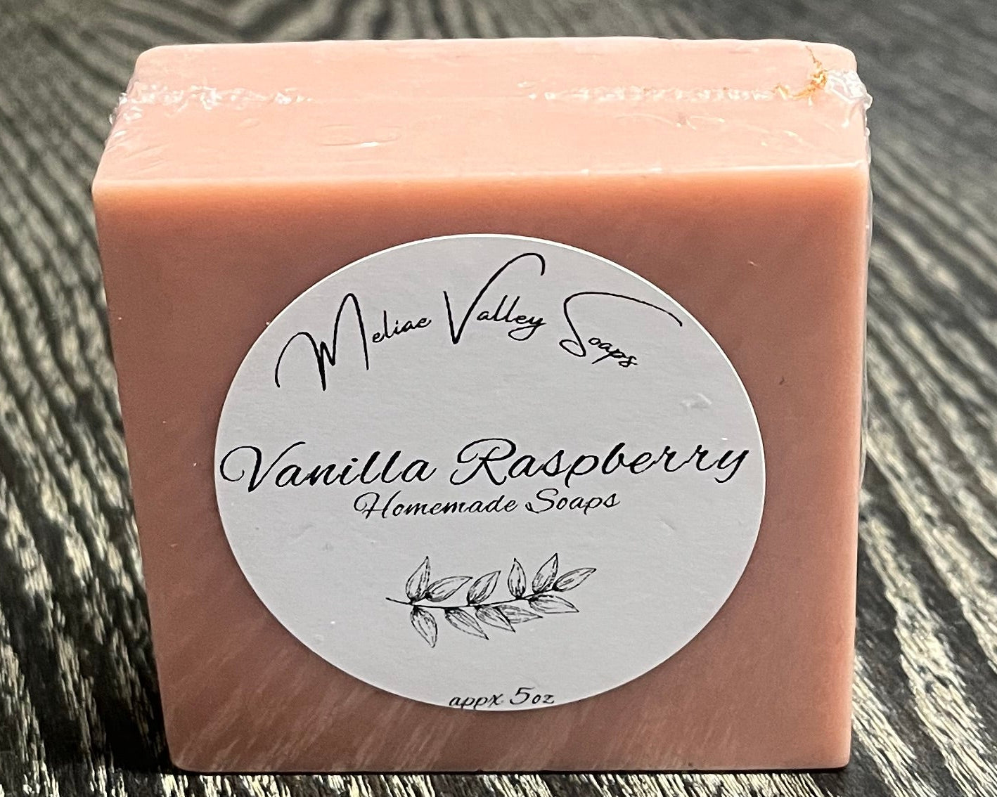 A pink bar of soap with a white label upright on a textured surface. 