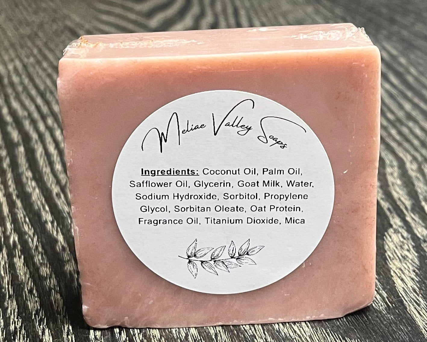 A pink bar of soap with a white ingredients label on a textured surface. 