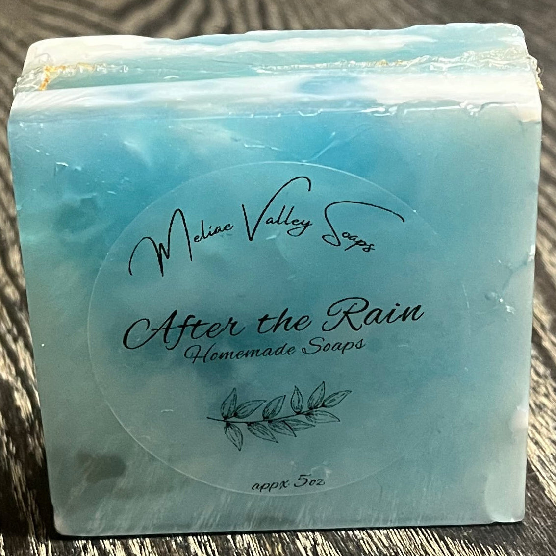 A multi colored, clear, white, and blue soap bar with a clear label. It is upright on its side, showing the top of the bar. 