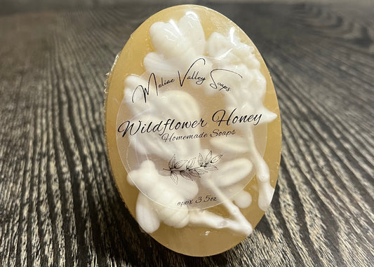 A bar of amber soap with a clear label. It is upright to show the white details on top of the bars. 