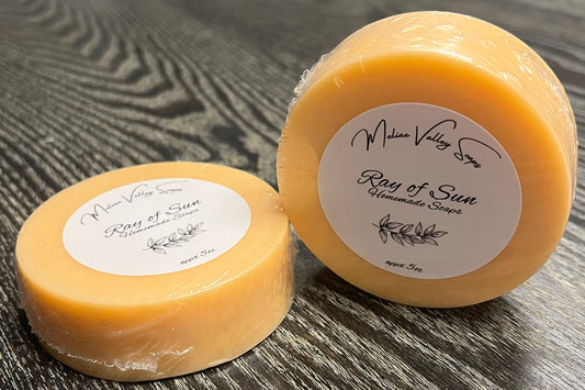 Two orange soaps with labels on a wooden surface.