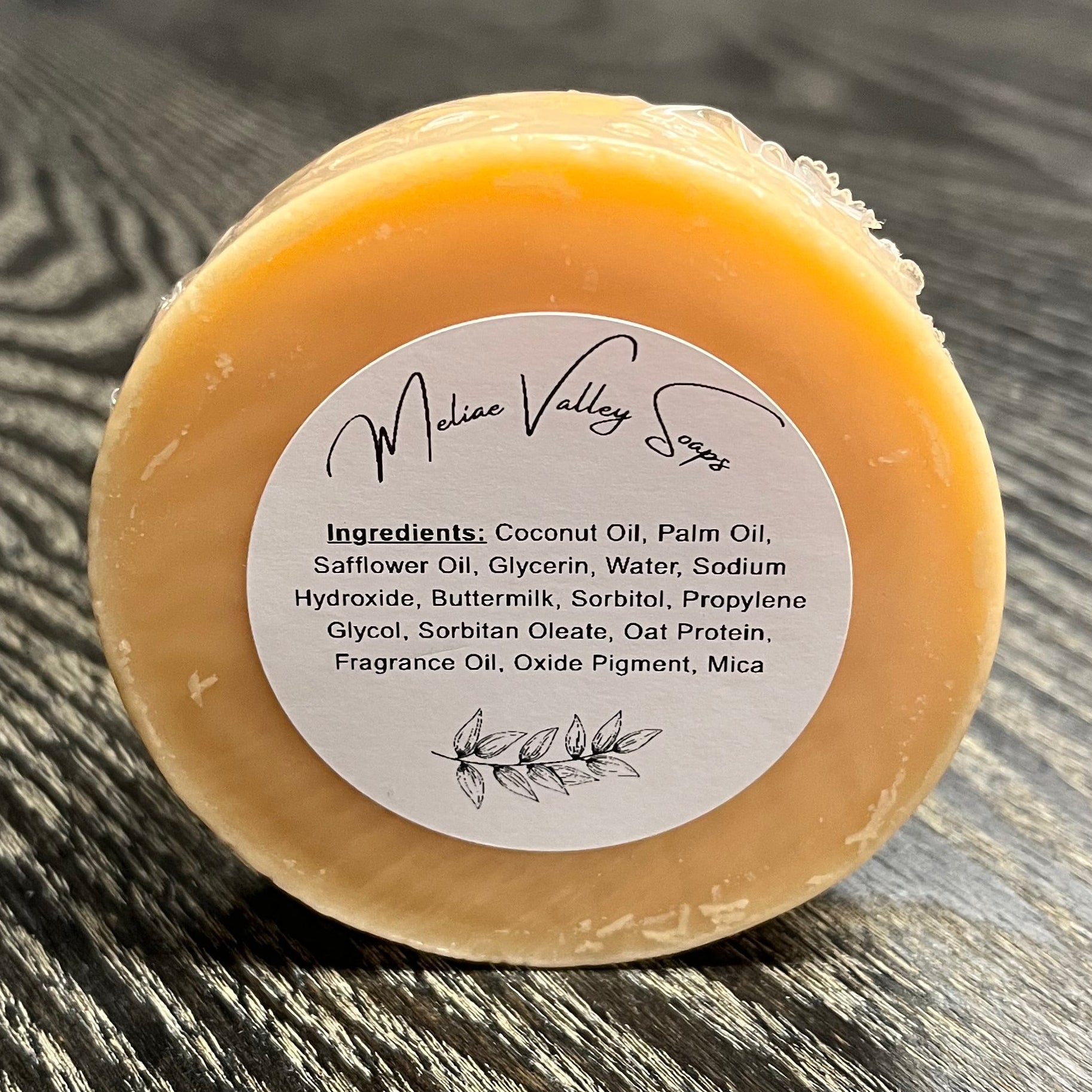 Bar of orange soap with a label on a wooden surface.
